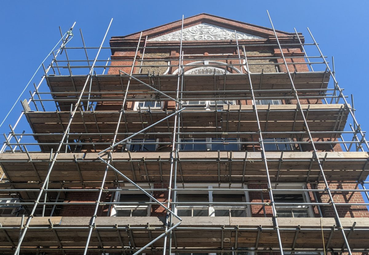 Metal scaffolding covers the front of a brick building under a clear blue sky.
