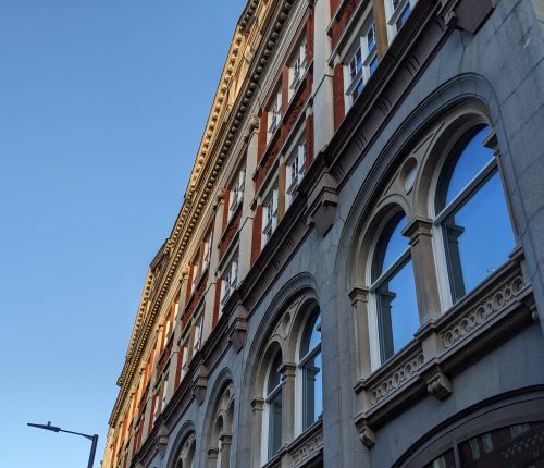 Red and gray buildings with arched windows under a clear blue sky, angled view accentuating their architectural details.