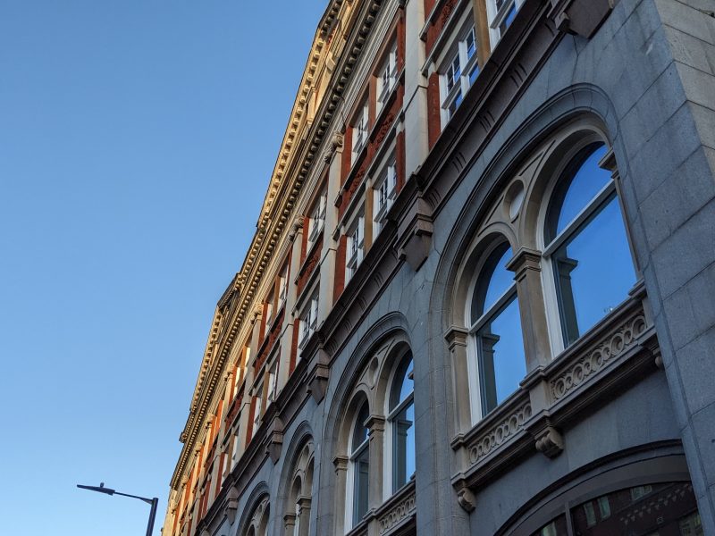 Red and gray buildings with arched windows under a clear blue sky, angled view accentuating their architectural details.