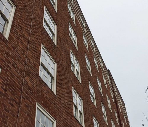 A red brick building with multiple white-framed timber sash windows under an overcast sky.