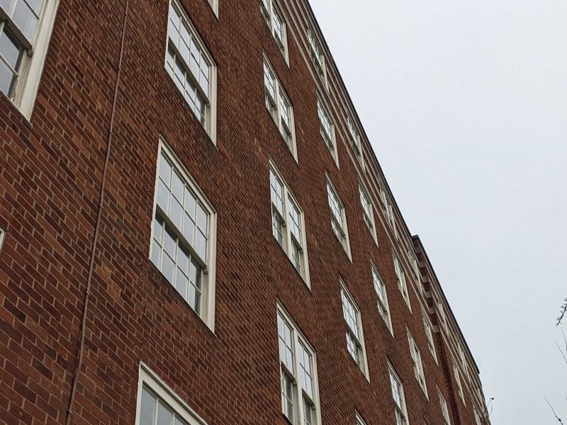 A red brick building with multiple white-framed timber sash windows under an overcast sky.