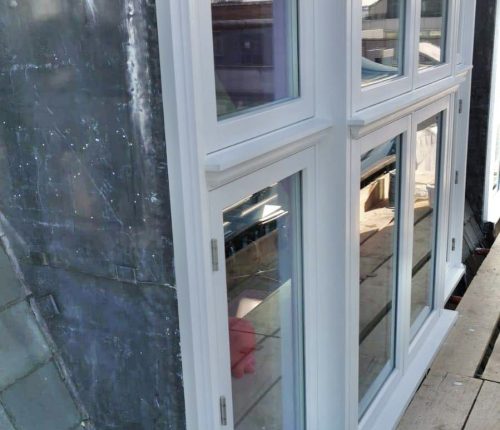 White double doors with glass panes are partially open, reflecting the sky, set against a building and paving stones.