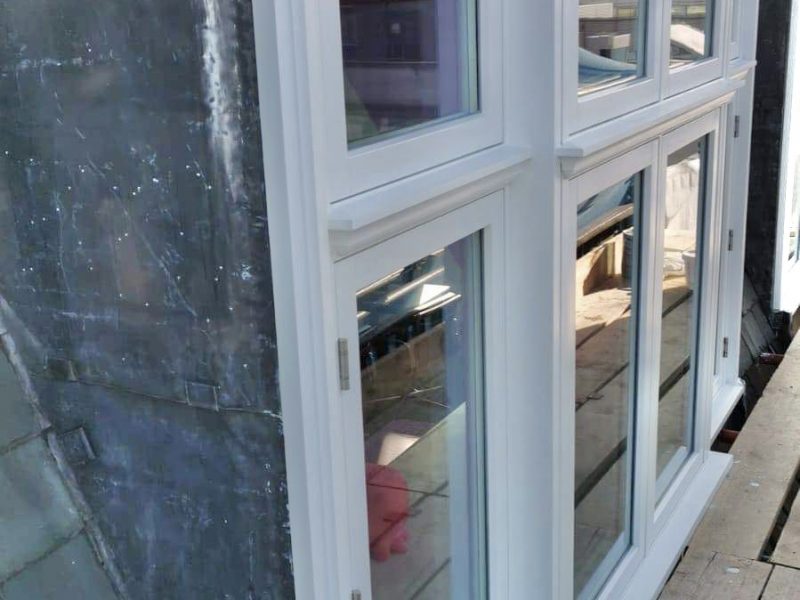 White double doors with glass panes are partially open, reflecting the sky, set against a building and paving stones.