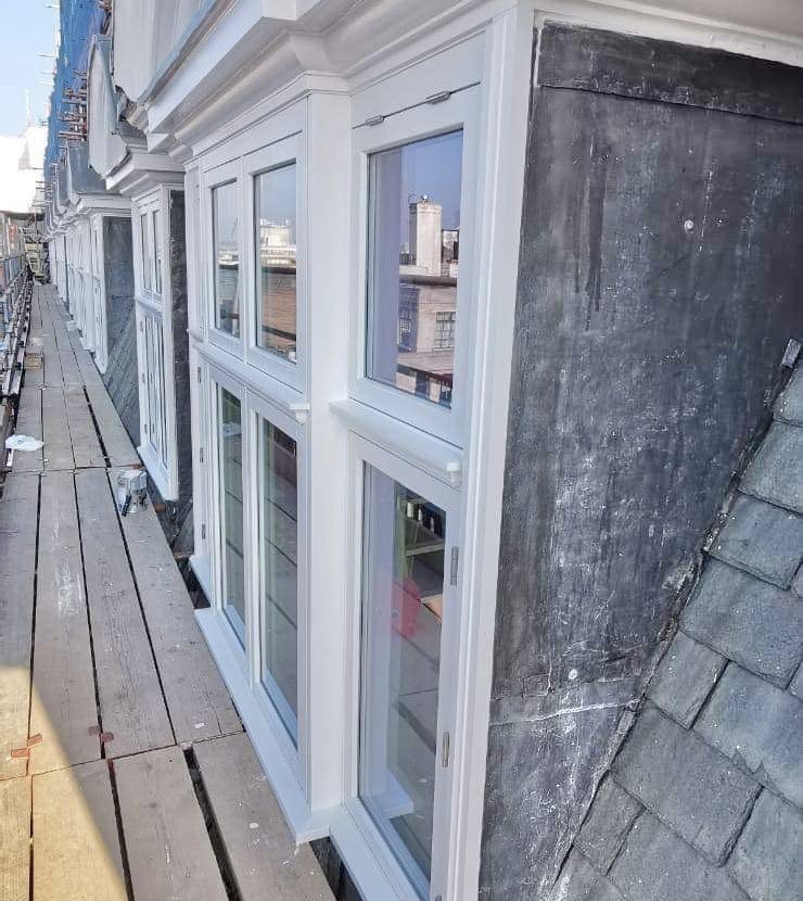 New white windows line along a building's side; they're adjacent to a gray slate roof.