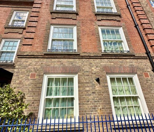 A multi-story brick building with white-framed windows, behind a blue fence under a clear sky.