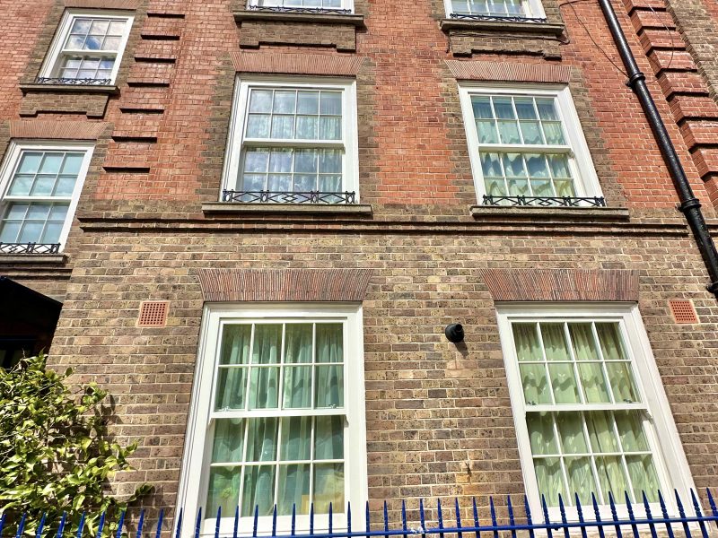 A multi-story brick building with white-framed windows, behind a blue fence under a clear sky.