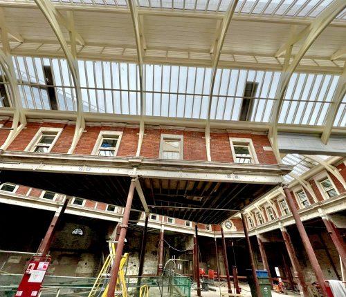 A red brick building under renovation with scaffolding, under a translucent roof, hinting at construction in an urban setting.