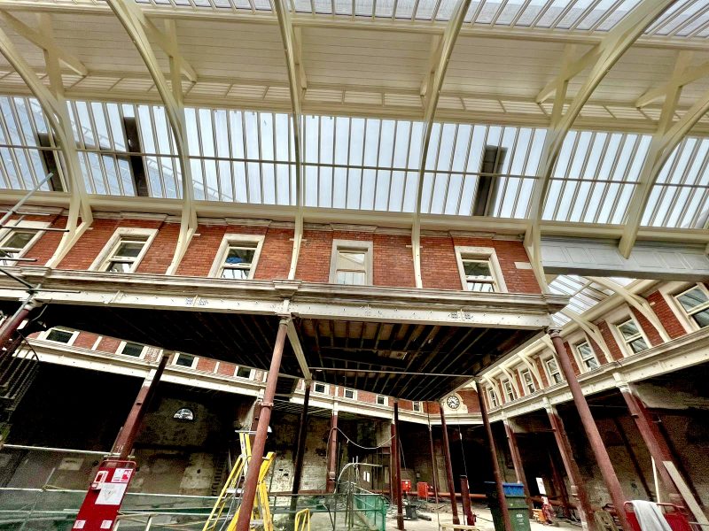 A red brick building under renovation with scaffolding, under a translucent roof, hinting at construction in an urban setting.