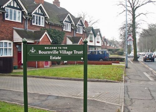 A sign for Bournville Village Trust Estate next to a pavement with terraced houses in the background