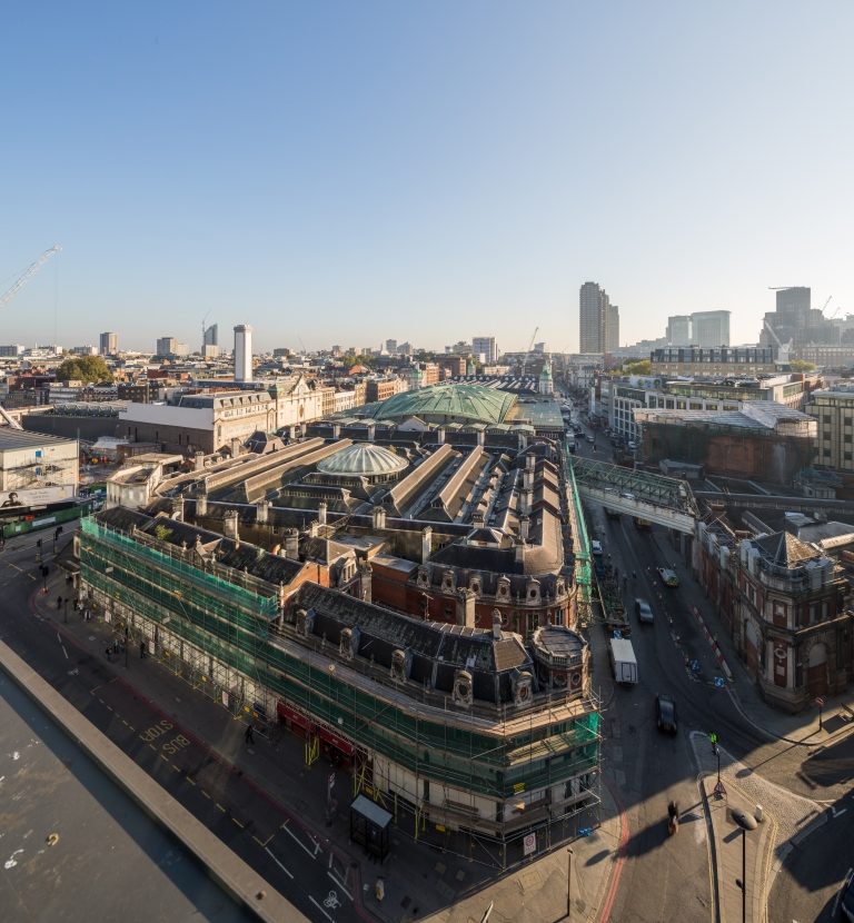 A historic building with a green rooftop is surrounded by urban infrastructure on a clear day, casting long shadows onto the street below.