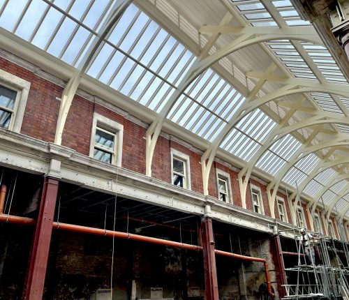 A Victorian-style brick building undergoing renovation, with visible scaffolding and a glass roof supported by arched white beams.