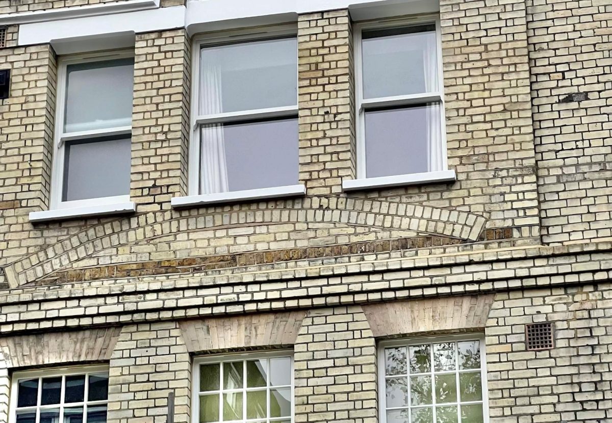 White-framed windows set in a brick building, there is a central arch design above them