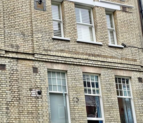 A brick building with multiple white-framed windows and a security camera attached to the wall; indicates an urban residential setting.