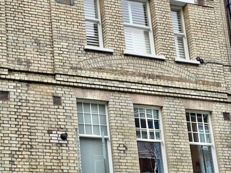 A brick building with multiple white-framed windows and a security camera attached to the wall; indicates an urban residential setting.