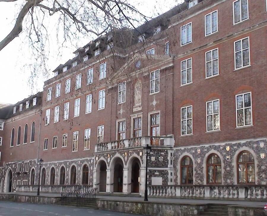 Wide view of the historic red brick Church House building's multi-story facade, featuring a stone arched lower level and central entrance balcony.