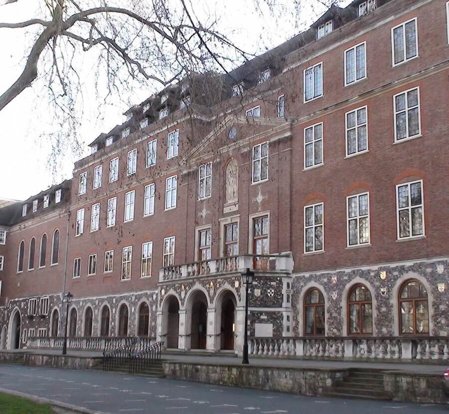 Wide view of the historic red brick Church House building's multi-story facade, featuring a stone arched lower level and central entrance balcony.