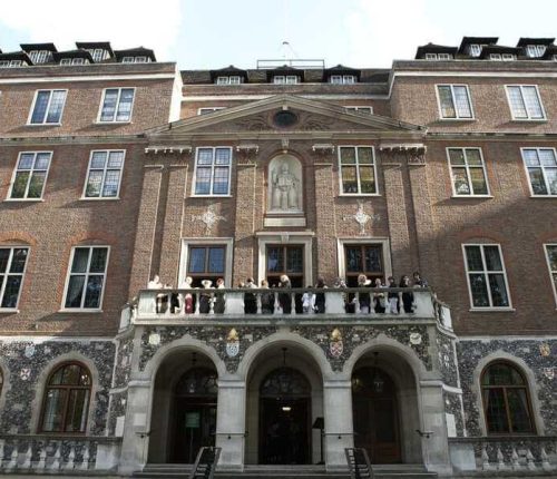Straight-on view of the main entrance of Church House with a central stone portico and balcony, where a group of people is standing.