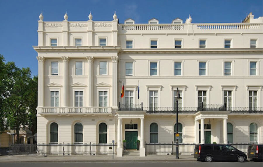 Close-up of the central part of the German Embassy in London, highlighting the main entrance, two flags, and the classical architectural details of the white facade.