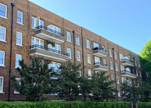 Side view of a multi-story, red brick apartment building featuring several rows of balconies with black railings and white window frames.
