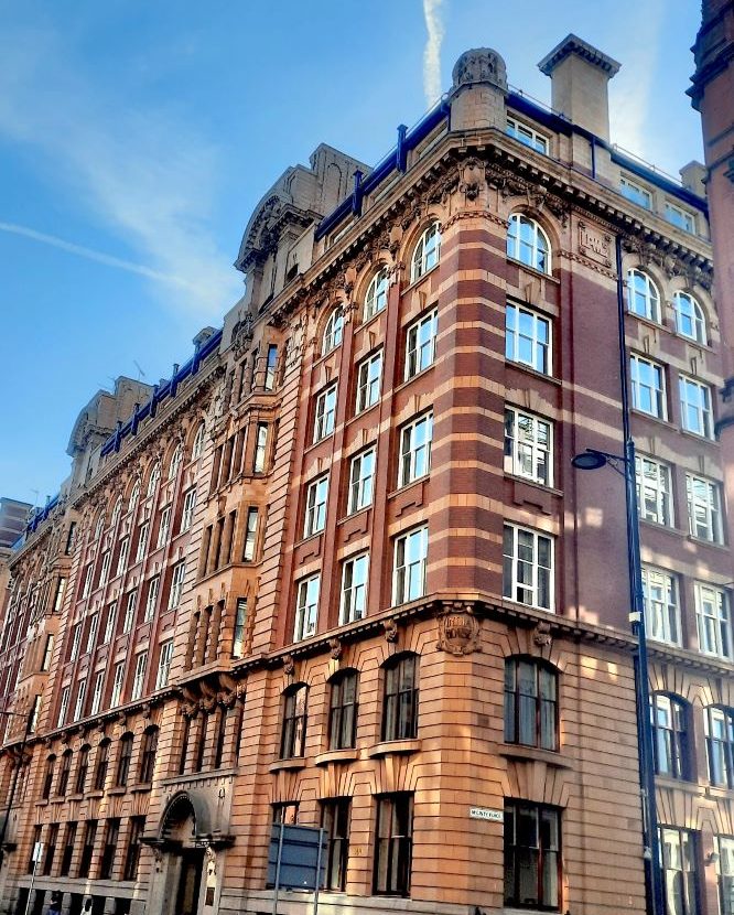 Historic India House - brick building with ornate detailing and large windows stands against a clear blue sky. Street lamps are visible nearby, highlighting the architectural features of the structure.