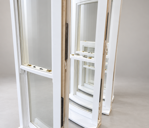 Profile view of four white timber sash windows arranged in a row against a plain studio background, detailing the wooden side profiles, brass sash locks, and internal counterweight systems.
